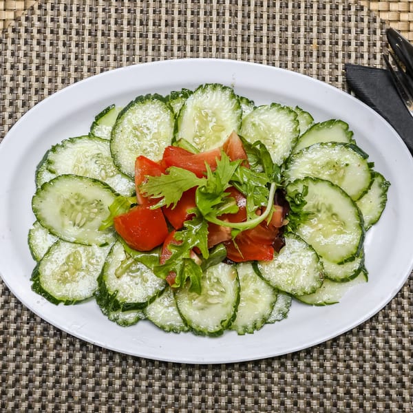 A fresh Jamaican cucumber salad with sliced cucumbers, diced tomatoes, and greens on a white plate.